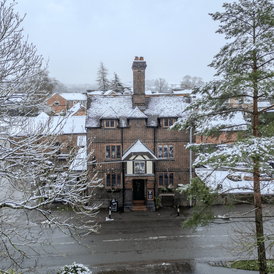 The exterior of The Offley Arms in Madeley, a traditional white-rendered country pub with black timber framing, featuring a large outdoor seating area with wooden picnic benches and a classic hanging brewery sign.